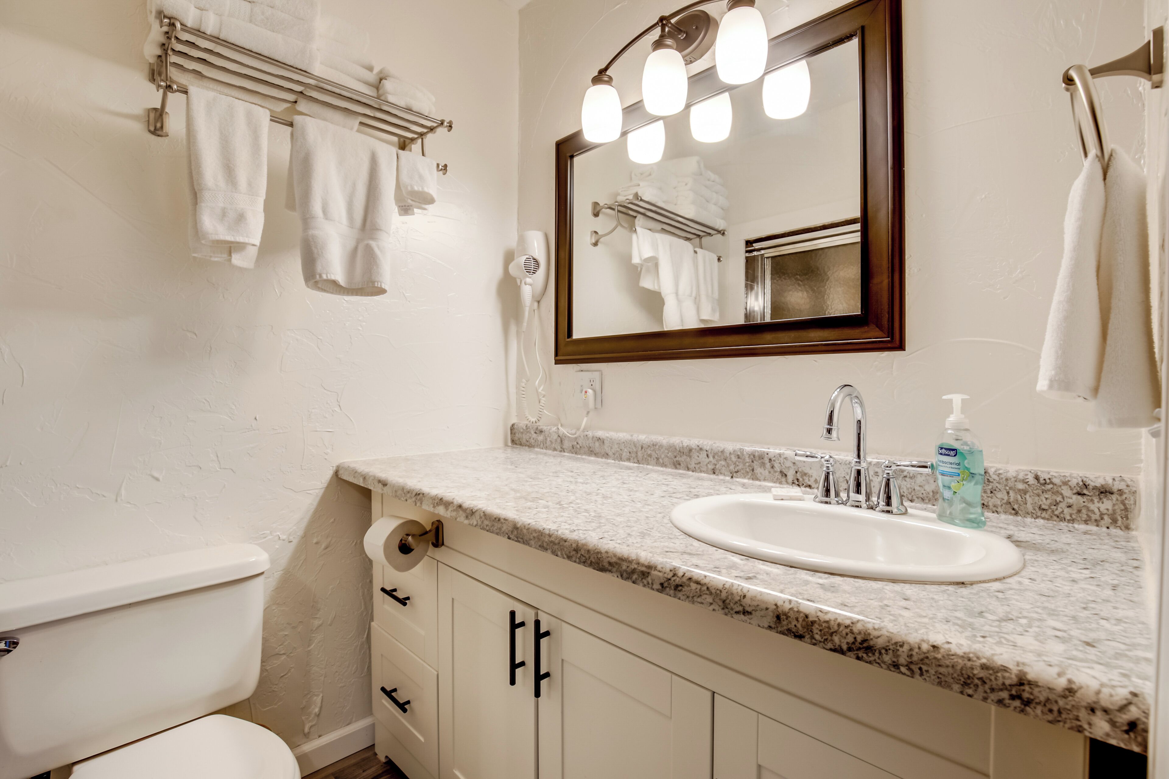 A bathroom with a white toilet, a sink with a mirror above it, and a towel rack with towels.