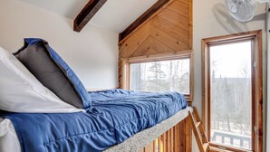A loft-style bedroom with a bunk bed, wooden beams, and a large window offering a view of trees. - Iron River Retreat w/ Sauna: Walk to Ski Brule! (Iron River)