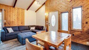 A cozy room with a wooden interior, a large window, a wooden dining table, and a sectional sofa. - Iron River Retreat w/ Sauna: Walk to Ski Brule! (Iron River)