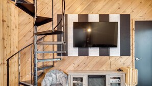 A room with a wooden floor, a TV mounted on the wall, a wooden cabinet, and a staircase. - Iron River Retreat w/ Sauna: Walk to Ski Brule! (Iron River)