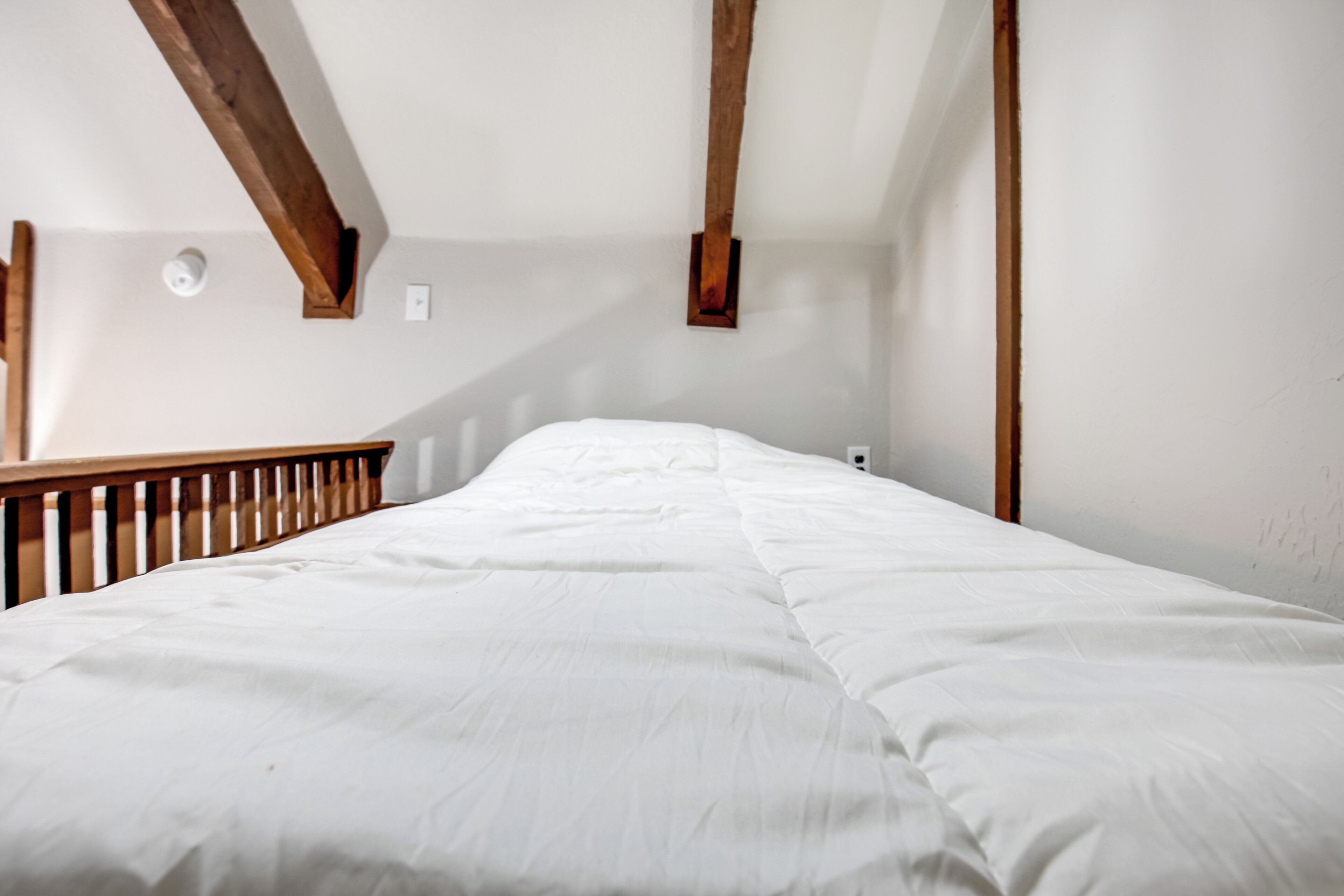 Un dormitorio con una cama grande, vigas de madera y una pared blanca.