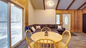 A cozy room with a wooden interior, a round table with chairs, a sofa with cushions, and a door with a frosted glass window. - Iron River Condo w/ Gas Grill Near Skiing + Hiking (Iron River)