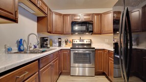 A kitchen with wooden cabinets, a stainless steel oven, a microwave, and a refrigerator. - Iron River Condo w/ Gas Grill Near Skiing + Hiking (Iron River)