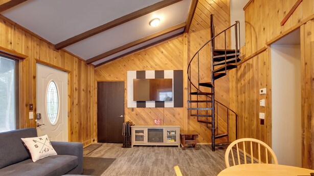 A cozy room with wooden walls, a sofa, a table, and a spiral staircase. - Iron River Condo w/ Gas Grill Near Skiing + Hiking (Iron River)