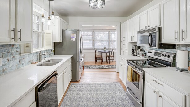 A modern kitchen with white cabinets, stainless steel appliances, and a dining area with a table and chairs. - Rossville Home Near Downtown & Lookout Mountain! (Rossville)