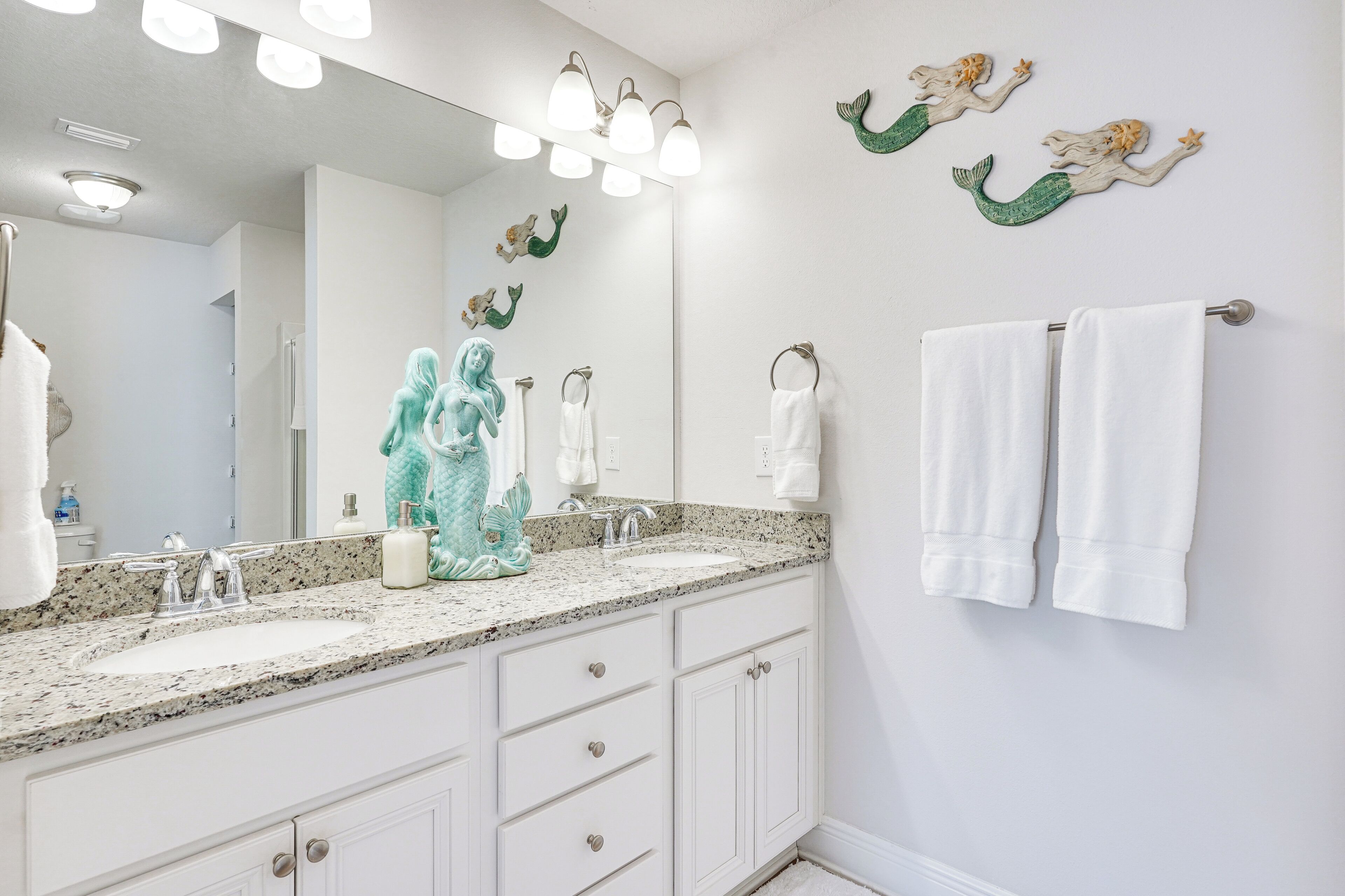 A bathroom with two sinks, a large mirror, and decorative mermaid wall art.