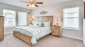 A bedroom with a wooden bed, two bedside tables, a ceiling fan, and large windows with blinds. - PCB Townhome w/ Deck & Pool Access: 3 Mi to Beach! (Panama City Beach)