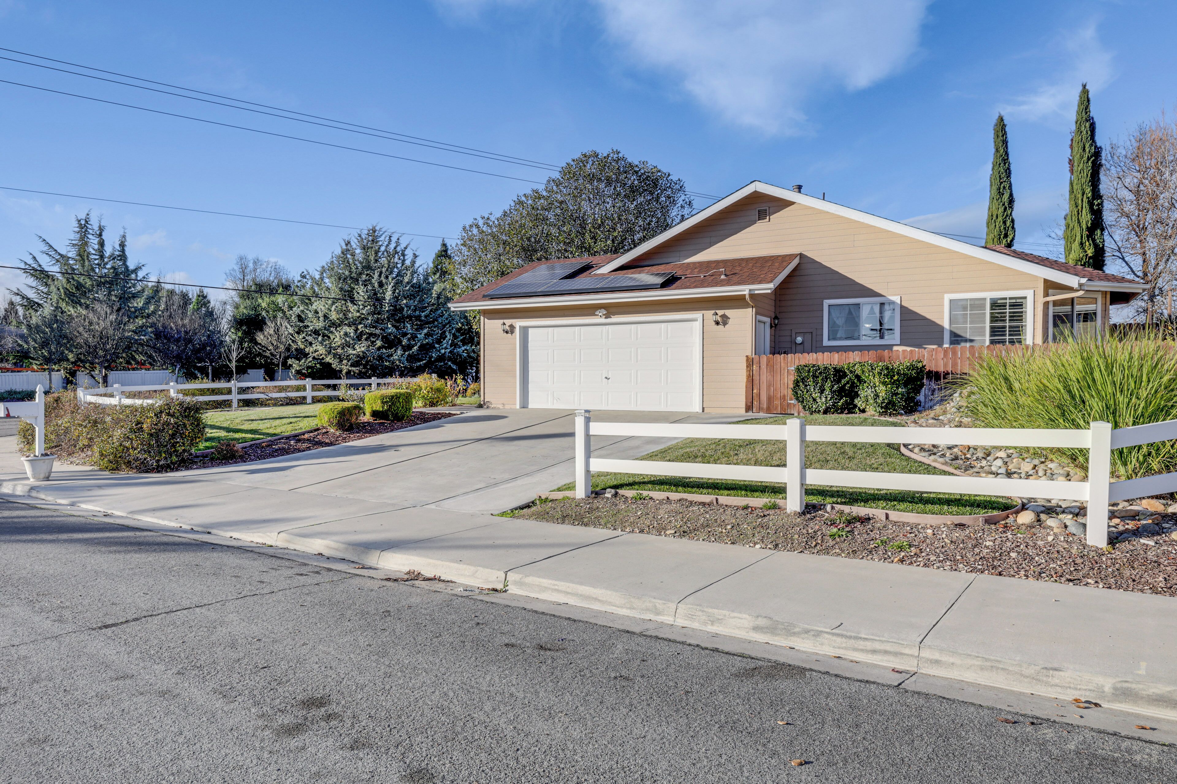 A single-story house with a garage, surrounded by a white fence, and a driveway leading to the front door.