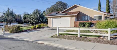 A single-story house with a garage, surrounded by a white fence, and a driveway leading to the front door.