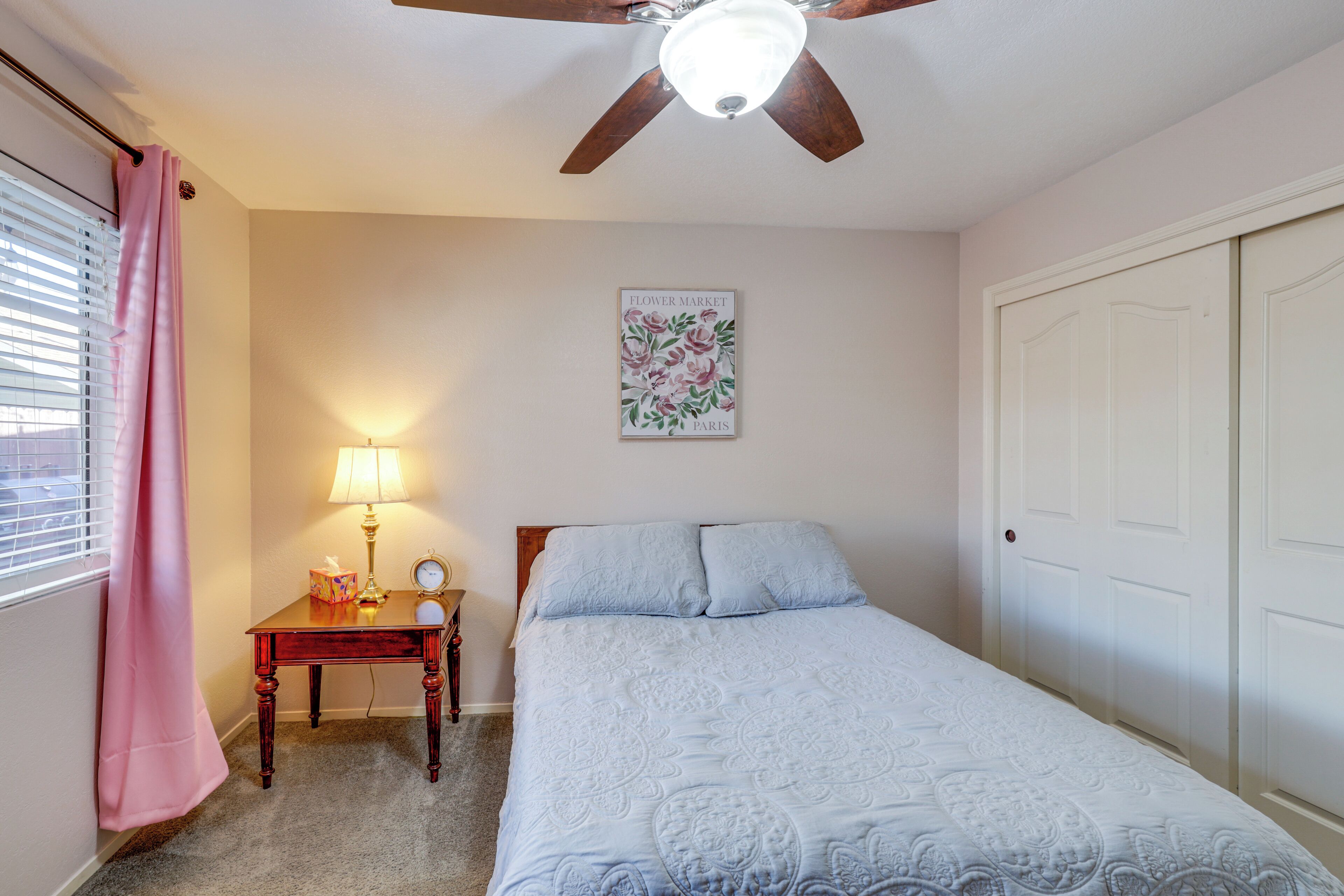 A bedroom with a bed, a nightstand, a lamp, a ceiling fan, and a door.