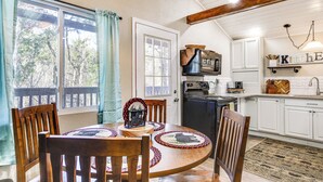 A dining area with a round wooden table, chairs, and a view of the outdoors through large windows. - Cozy Cottage w/ Pool Btwn Knoxville & Pigeon Forge (Kodak)