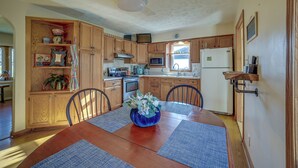 A kitchen with wooden cabinets, a dining table with placemats, a microwave, a stove, and a refrigerator. - Quaint Youngstown Home ~ 2 Mi to Boardman Park! (Poland)