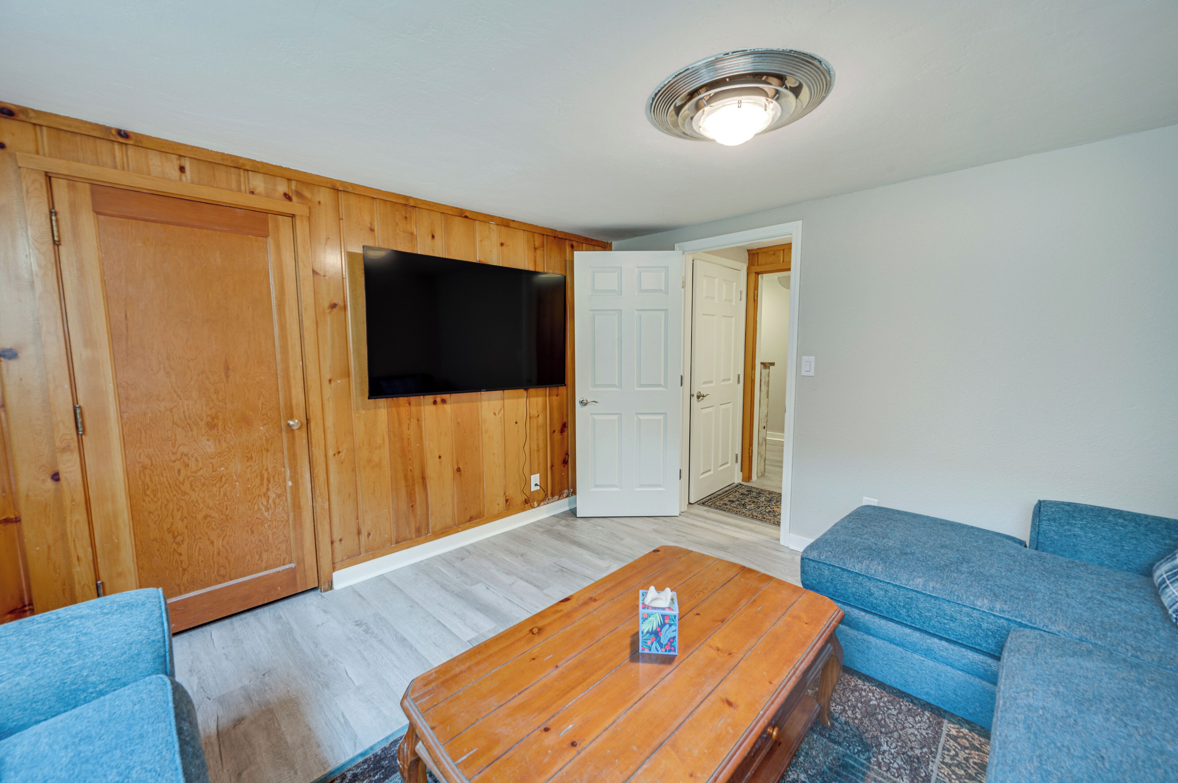 Un salon avec un mur en bois, un téléviseur à écran plat, un canapé bleu et une table basse en bois.