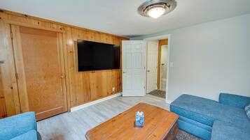 Un salon avec un mur en bois, un téléviseur à écran plat, un canapé bleu et une table basse en bois.