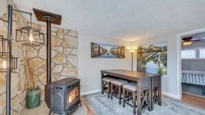 Une pièce chaleureuse avec un mur en pierre, un poêle à bois, une table à manger avec des chaises et des œuvres d’art accrochées aux murs.