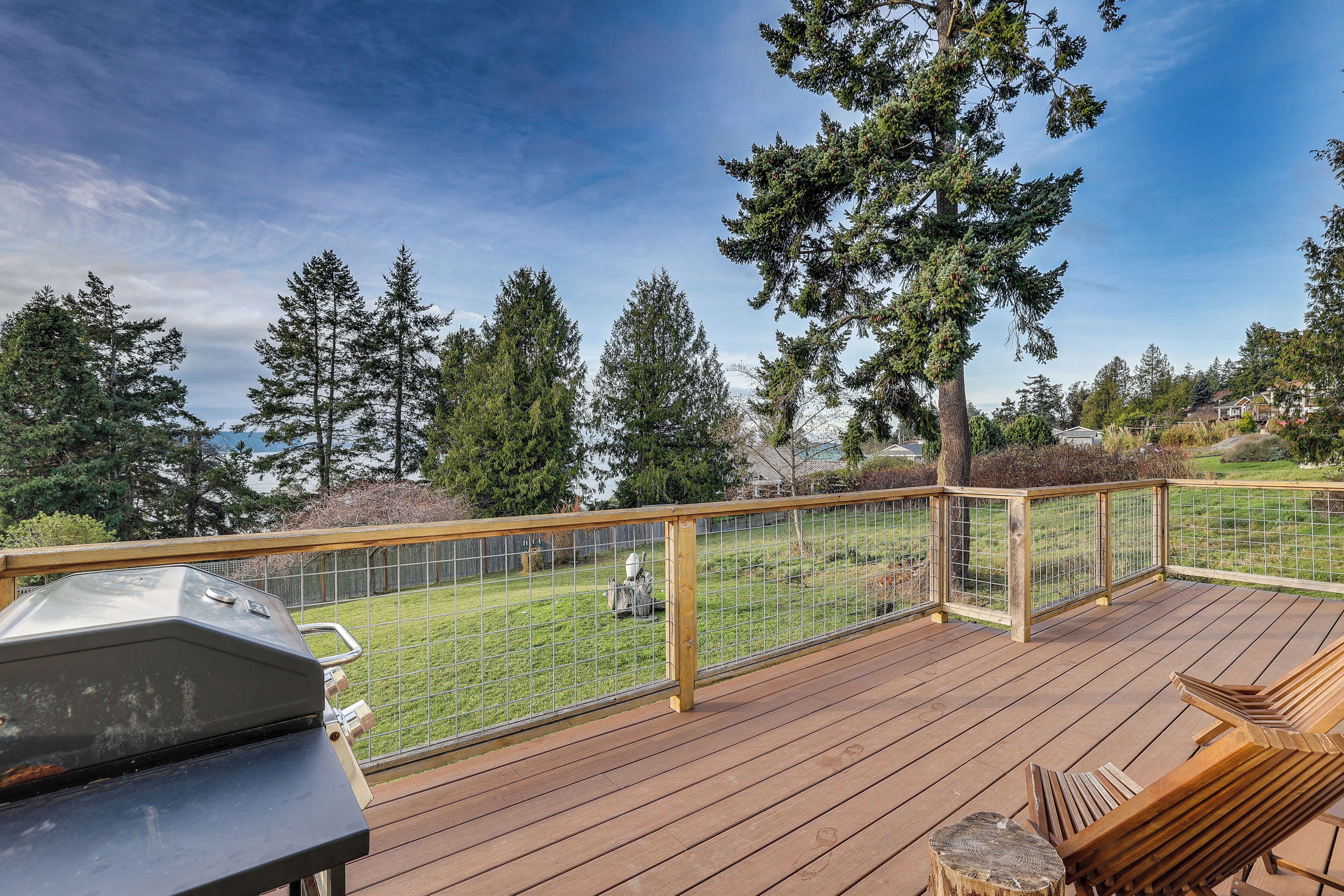 Una terraza con una parrilla, sillas de madera y vistas a un jardín con árboles.