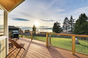 Une terrasse en bois avec un barbecue et des chaises, donnant sur une pelouse et un lac.