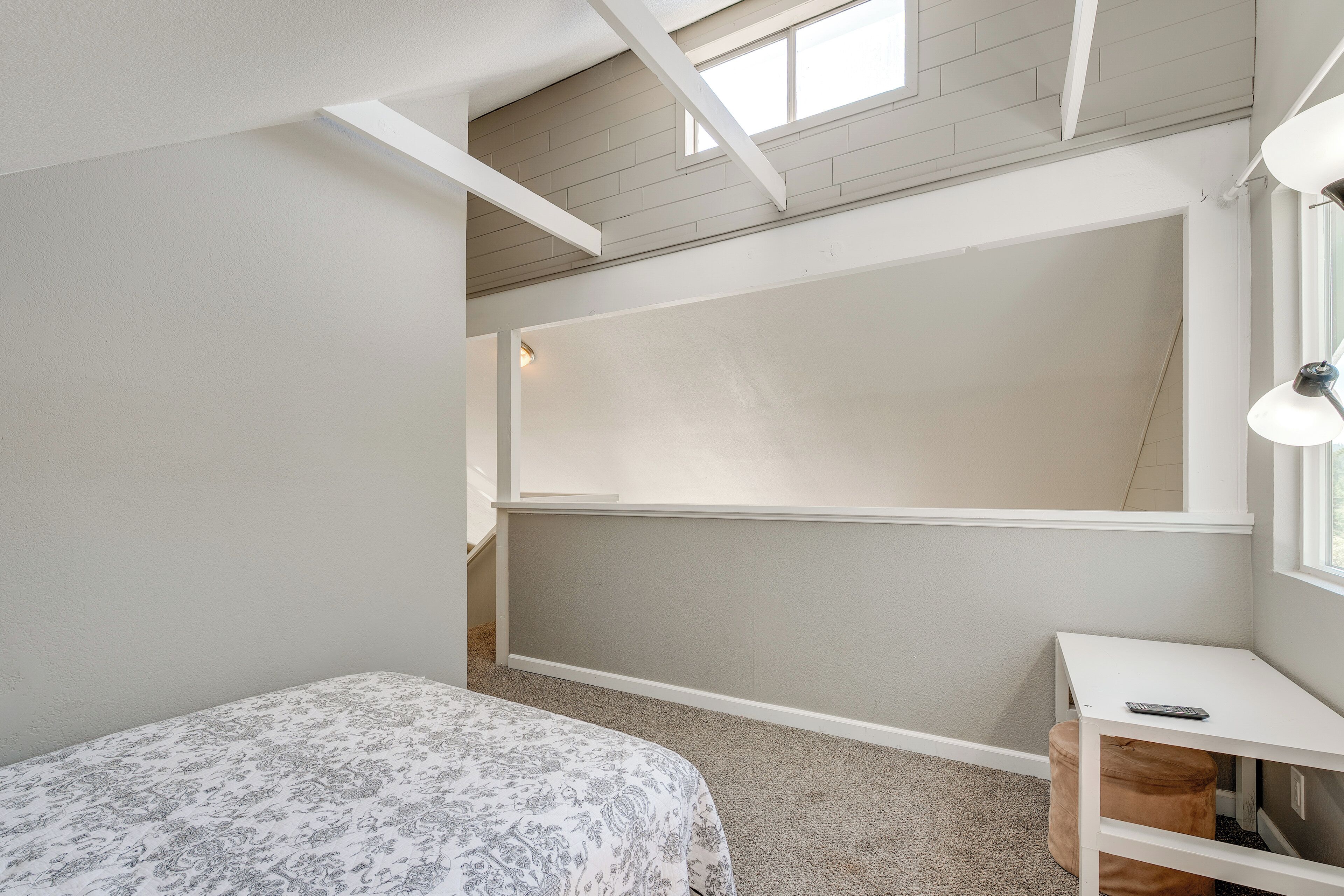 Un dormitorio con cama, escritorio, ventana y techo con vigas a la vista.