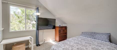 A bedroom with a bed, a desk, a chair, a dresser, and a window with a view of trees.