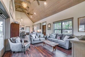 Relax in this spacious living area with a high ceiling and exposed beams, featuring a large sofa set, coffee table, and dining area with a kitchen.