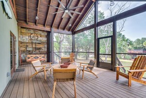 A wooden deck with wicker furniture, a ceiling fan, and large windows overlooking a natural landscape.