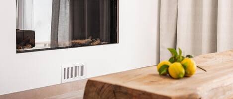 Una habitación moderna con una mesa de madera, chimenea empotrada y una ventana con cortinas.