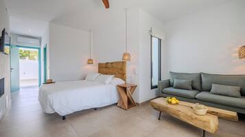 A modern bedroom with a bed, bedside table, and a wooden headboard. There is a sofa and a wooden bench with a basket and lemons on it.