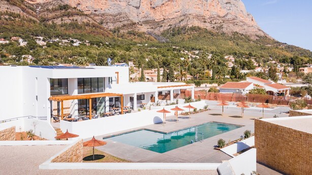Un hotel moderno con piscina, mobiliario exterior y vistas a una montaña.
