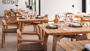 Un restaurante con mesas y sillas de madera, cada conjunto con platos, cubiertos y copas de vino.