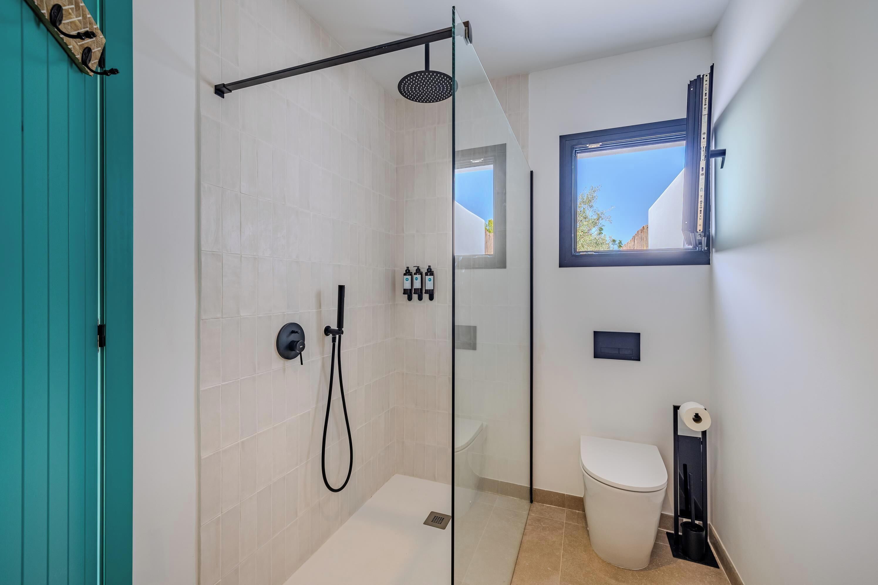 A modern bathroom with a glass-enclosed shower, a toilet, and a window.
