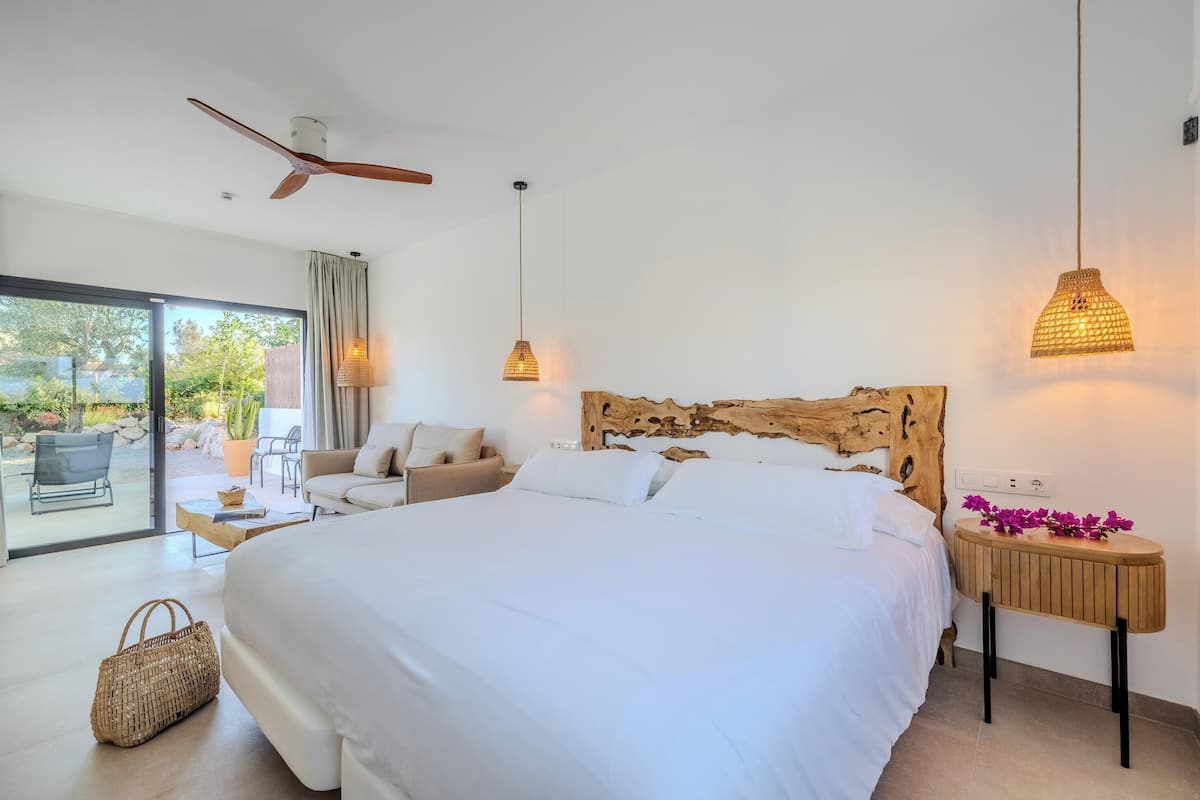 Quarto moderno com uma cama grande, cabeceira de madeira, ventilador de teto e vista para o exterior.
