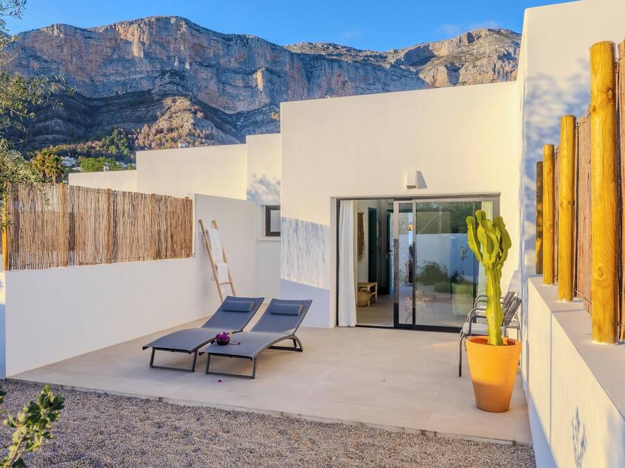 Un patio moderno al aire libre con dos sillones, un cactus en maceta y montañas al fondo.