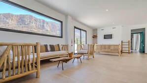 Amplia habitación con un ventanal que ofrece vistas a una cordillera, una mesa de centro de madera y dos bancos de madera.