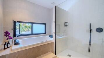 A modern bathroom with a bathtub, a glass-enclosed shower, and a window providing a view of greenery outside.