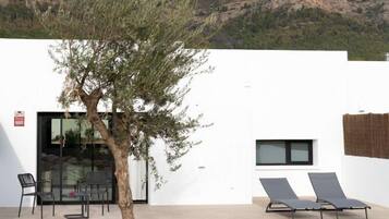 A modern building with a white exterior, a tree in the foreground, and a mountain in the background.