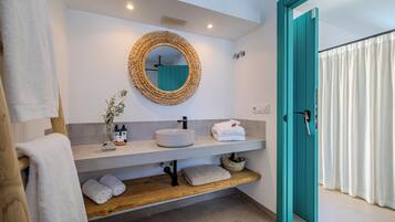 Un baño moderno con un espejo redondo, lavamanos blanco y puerta verde azulada.