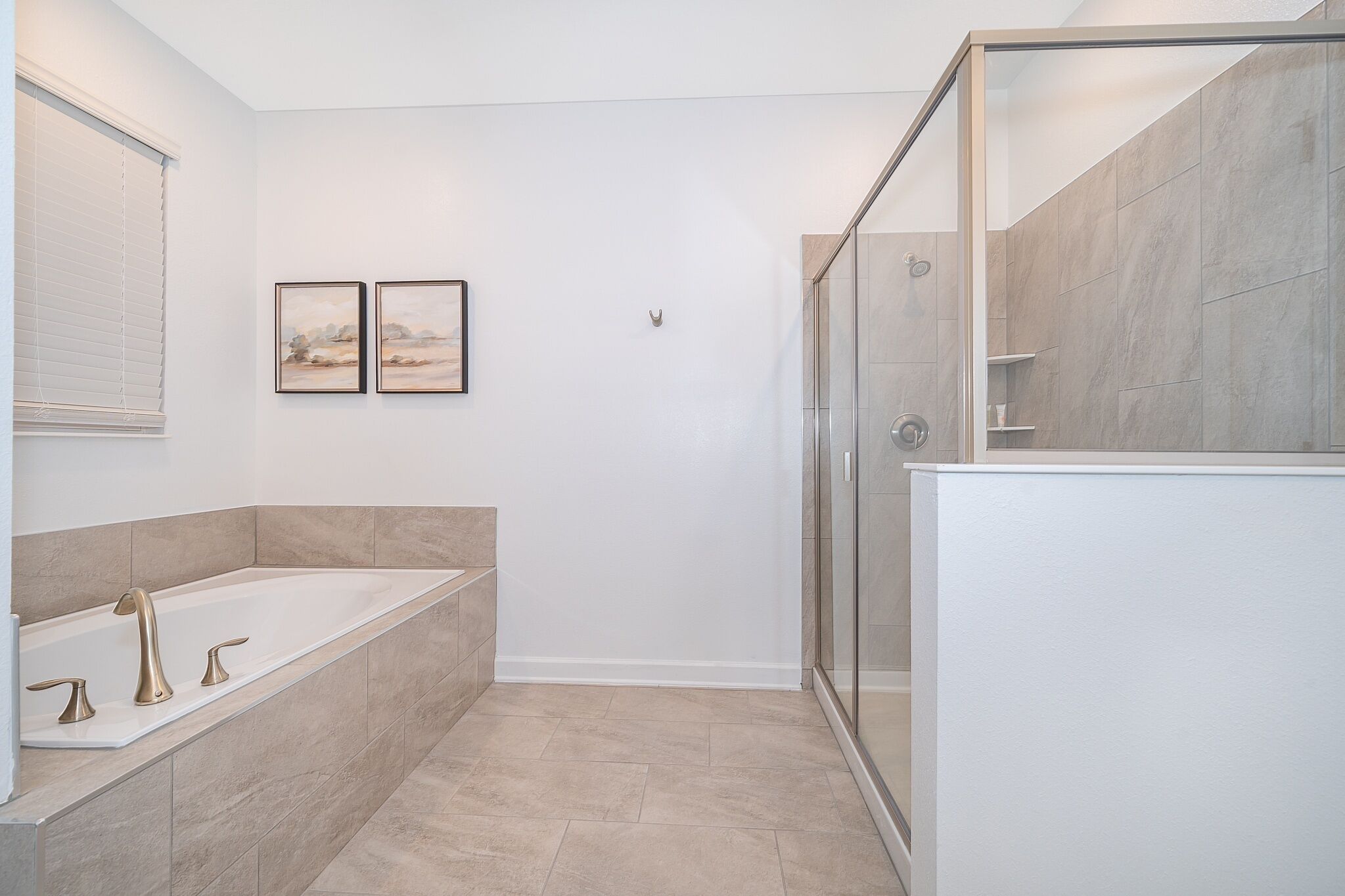 Un baño moderno con una bañera independiente, una ducha con mampara de vidrio y dos cuadros de paisajes enmarcados en la pared.