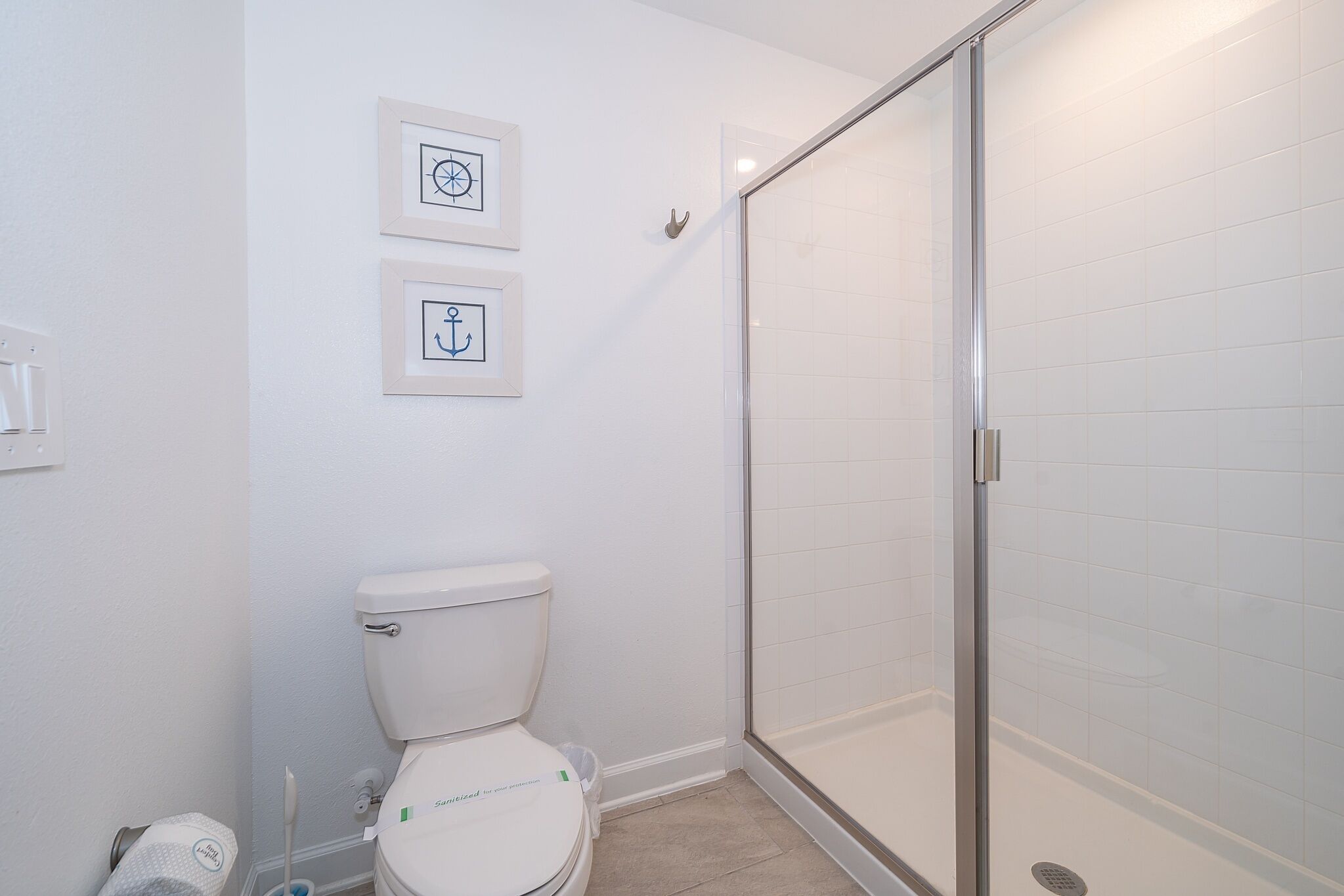 A bathroom with a toilet, a glass shower enclosure, and two framed pictures on the wall.