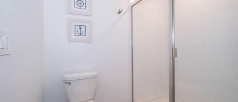 A bathroom with a toilet, a glass shower enclosure, and two framed pictures on the wall.