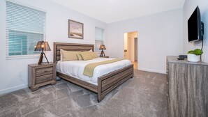 A bedroom with a wooden bed, bedside lamps, a flat-screen TV, and a small plant on a cabinet. - 9056sh-the Retreat At Championsgate 8 Bedroom Home by RedAwning (Davenport)