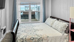Ein Schlafzimmer mit Bett, Fernseher, einem Fenster mit Vorhängen und Meerblick.