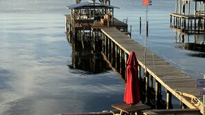 Eine Steg, der in ruhiges Wasser führt, mit überdachter Sitzgelegenheit und einem roten Sonnenschirm.