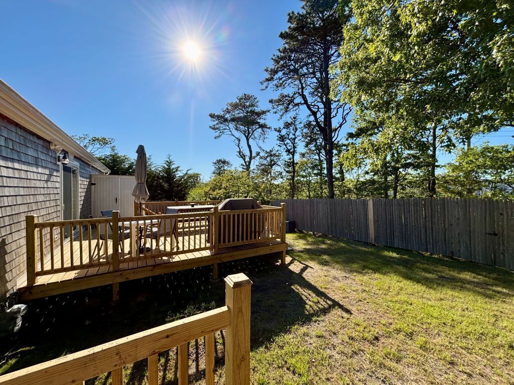 Eine Holzterrasse mit Gartenmöbeln, ein eingezäunter Garten und ein Haus im Hintergrund.