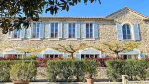 A stone building with multiple windows and shutters, surrounded by well-maintained hedges and potted plants. - Bastide du Soleil - 2-room apartment of 38m2 with terrace (CANNES)