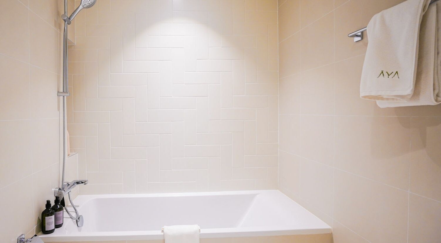 Une salle de bain moderne avec une baignoire blanche, une pomme de douche et un porte-serviettes sur lequel est posée une serviette.