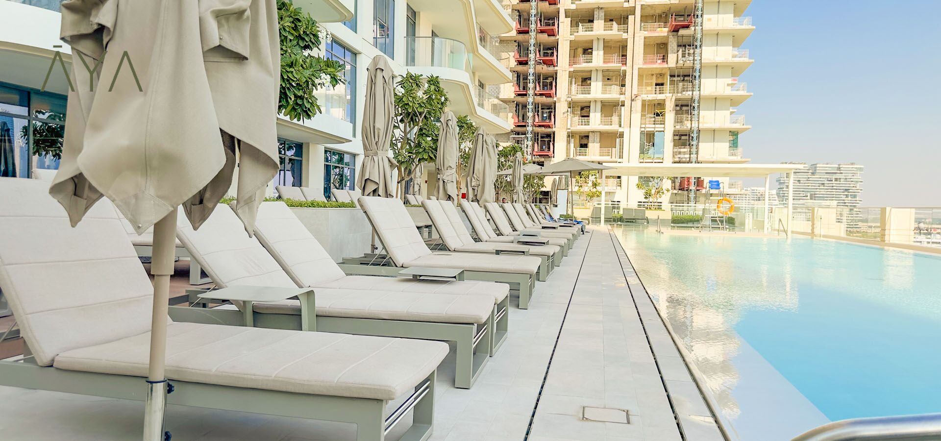 A row of sun loungers by a swimming pool with a view of a high-rise building in the background.