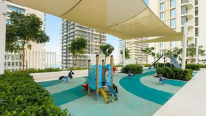 A playground with various play equipment, surrounded by greenery and a covered seating area. - Aya - Beachfront Apartment With all Amenities and Pool (Dubai)