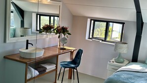 A modern bedroom with a sloped ceiling, a large mirror, a bedside table with a lamp, a chair, and a bed. - World of Horses Flats - Lucky (Stellenbosch)
