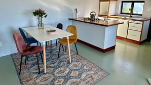 A modern kitchen with a central island, a dining area with a table and chairs, and a large window providing natural light. - World of Horses Flats - Lucky (Stellenbosch)