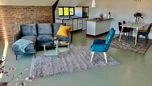 Un espace de vie moderne comprenant un canapé, une table basse et un fauteuil bleu. On y trouve également un coin cuisine avec une table à manger et des chaises.